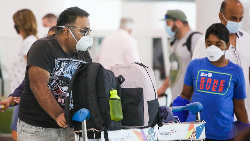 A man wearing a mask and a black shirt pushes a trolley with backpacks on it.