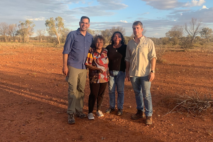 A group of people smiling at the camera in a red, rocky paddock near Thargomidah