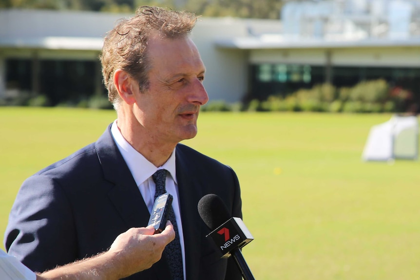 Foto tengah CEO Perth Glory Tony Pignata mengenakan jas dan dasi berbicara di depan mikrofon di atas oval.