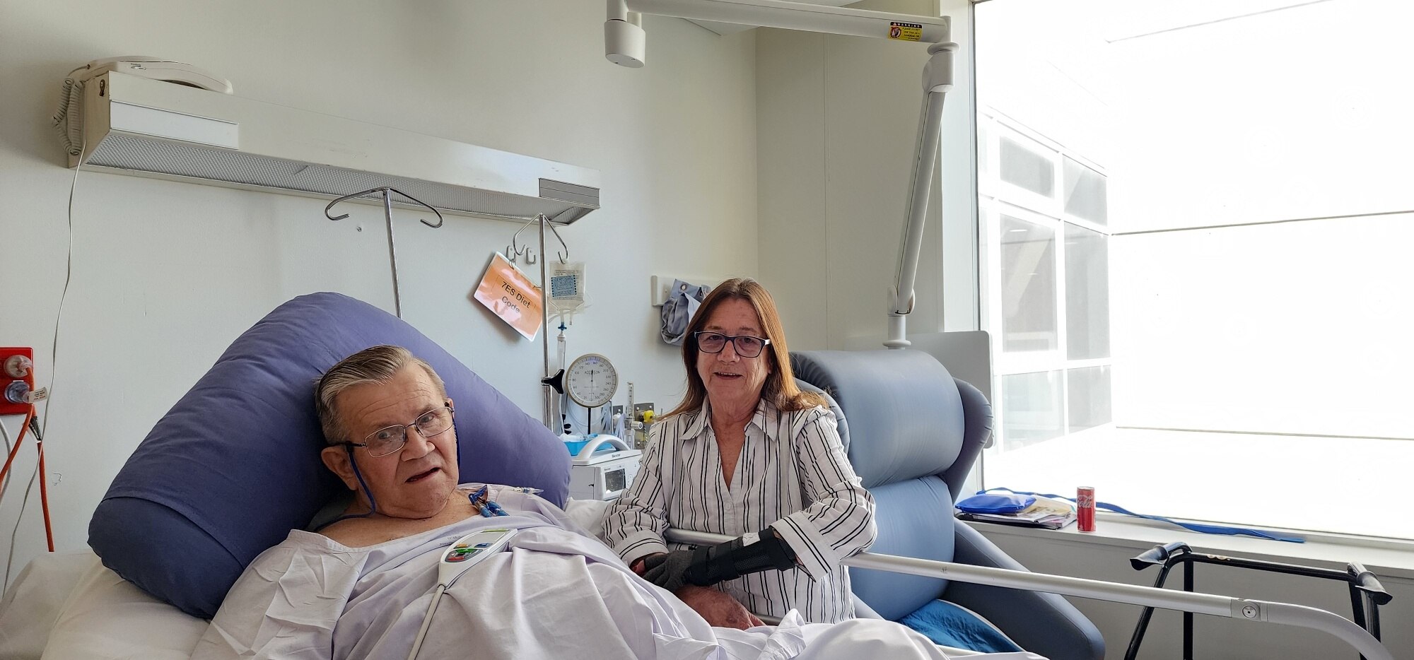 a photo of a man in a hospital bed with his wife sitting next to him 
