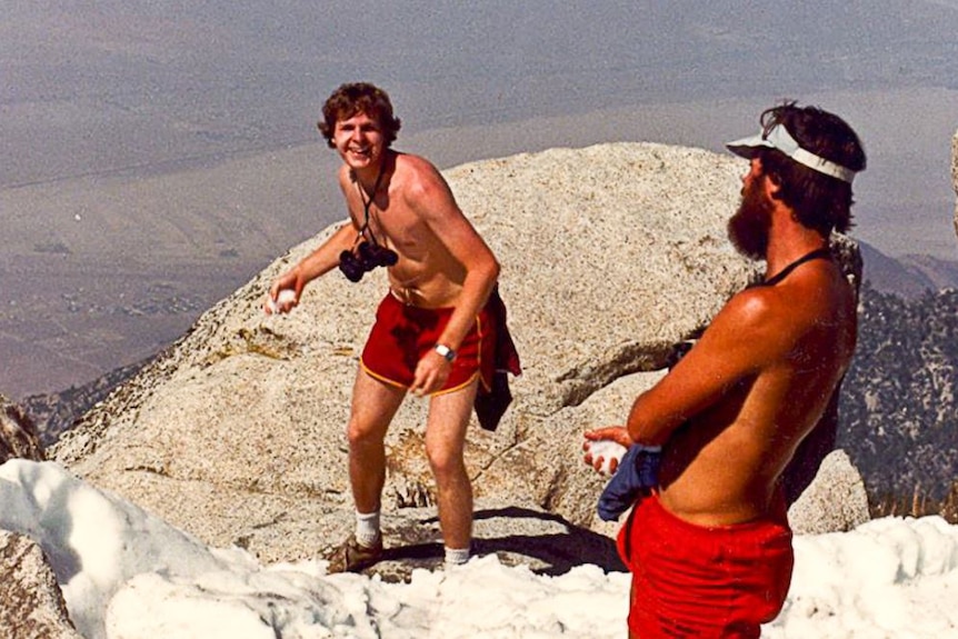 A 1982 photograph of a young man wearing shorts and no shirt holding a snowball high on a mountain