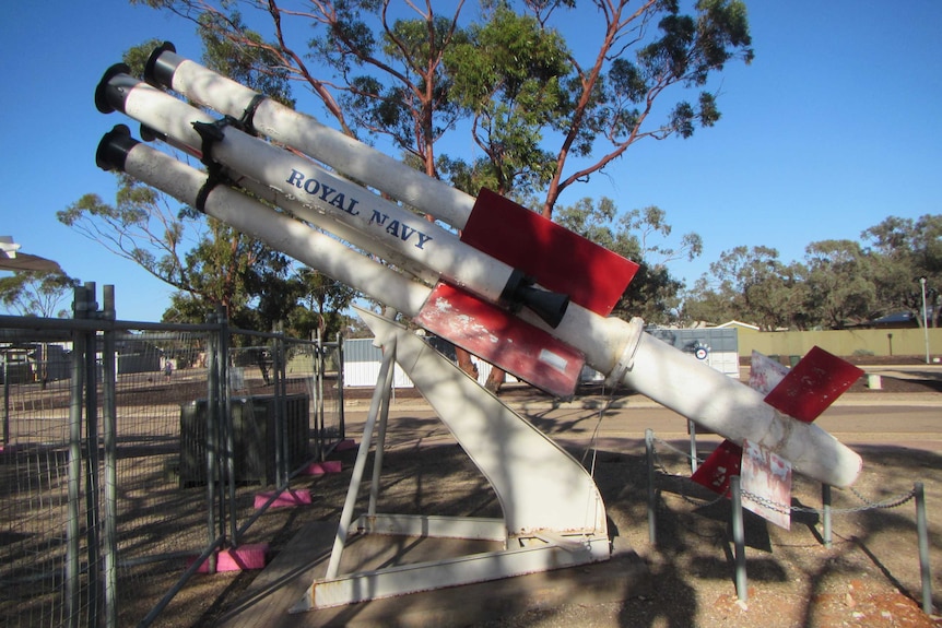 A four-cylinder white missile with red wing flaps sits on brown dirt.