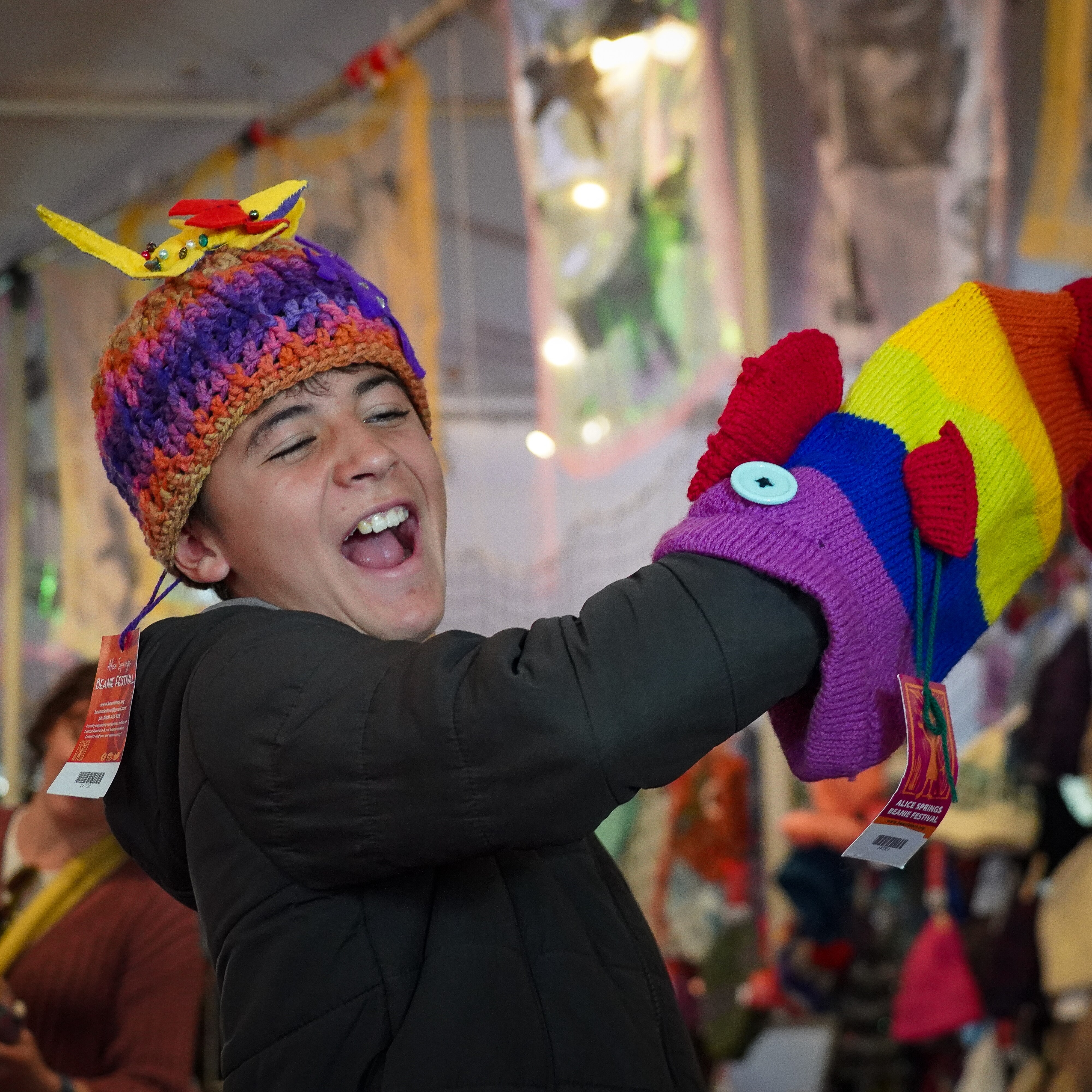 A boy holds a colourful knitted fish while wearing a handmade beanie, which has small yellow creature stitched on the top.
