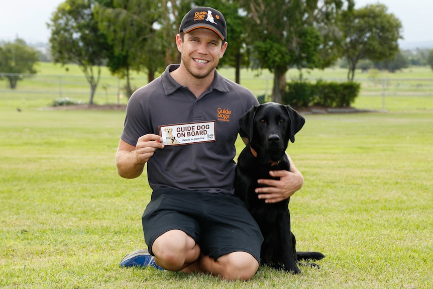 Guide Dog trainer holds a bumper stickers with a Guide Dog by his side.