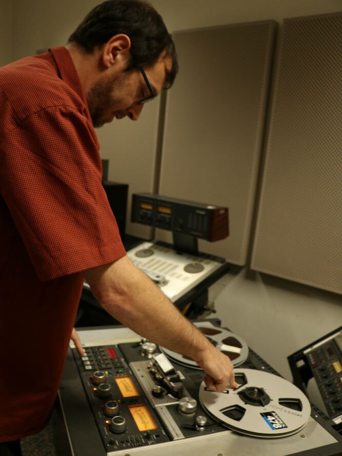 Jon Steiner operating reel to reel tape recorder with quarter inch tape threaded through it.