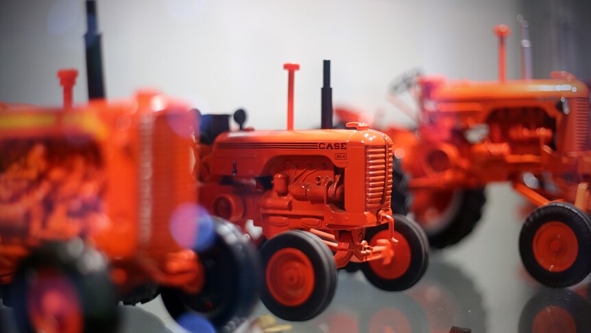 A Case model tractor sits on a shelf among many other orange tractors.