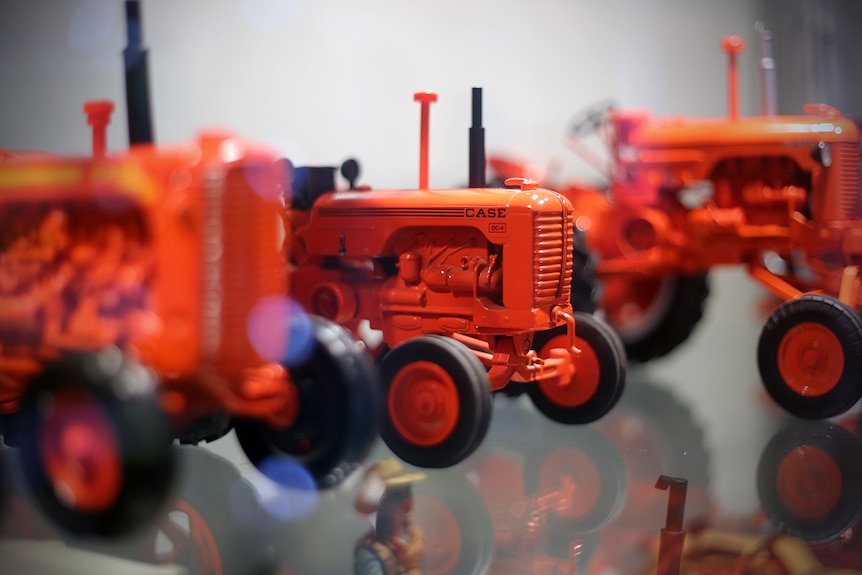 A Case model tractor sits on a shelf among many other orange tractors.