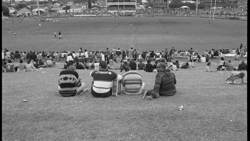 shot from behind of four Aboriginal men sitting down looking at a rugby legue oval