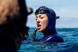 A close-up shot of a woman in a wetsuit and snorkel in the ocean.