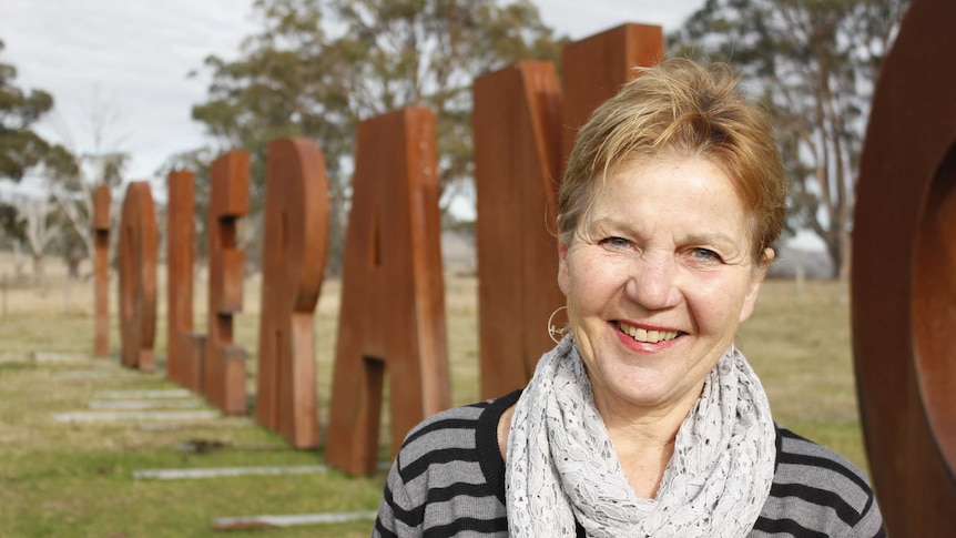 A woman stands in front of huge metal letters, spelling out the word tolerance in a paddock.