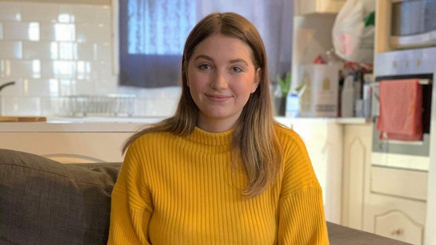 Young woman sits on a couch smiling