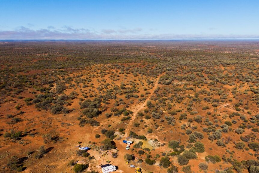 A wide aerial shot showing a remote, sparsely vegetated outback setting with gold dirt