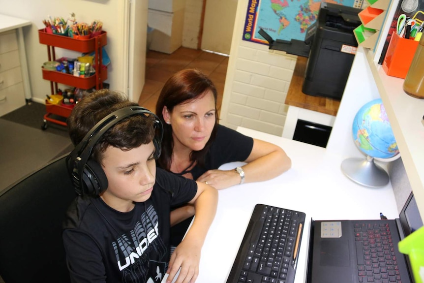 Amanda Steptoe looks on as her 12-year-old son Jack works at a desk on a computer for his distance education school work.