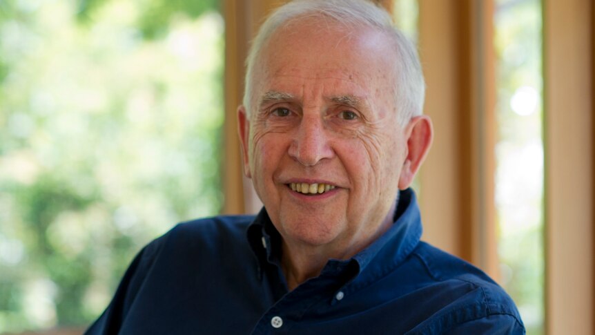 Author Hugh Mackay in a dark blue shirt smiling and sitting in front of a window