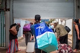 A group of people, carrying bags, leave a homeless shelter through a roller door.