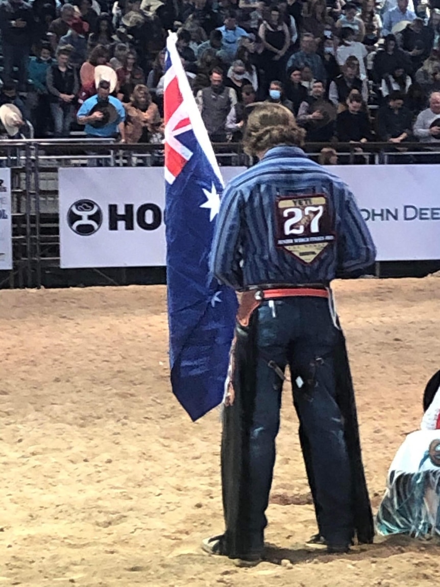 Teenager stand in the middle of the rodeo arena holding Australian flag