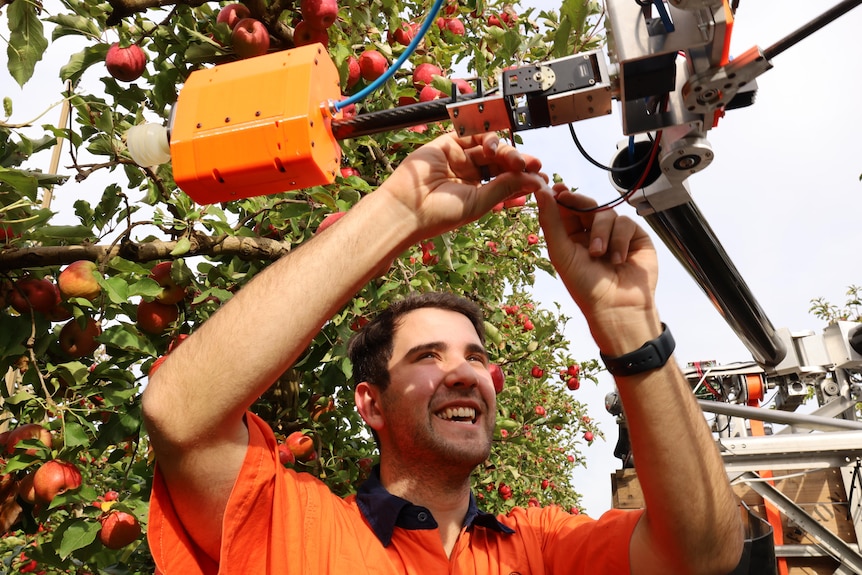 A man in orange high-vis is conecting cables on a robot