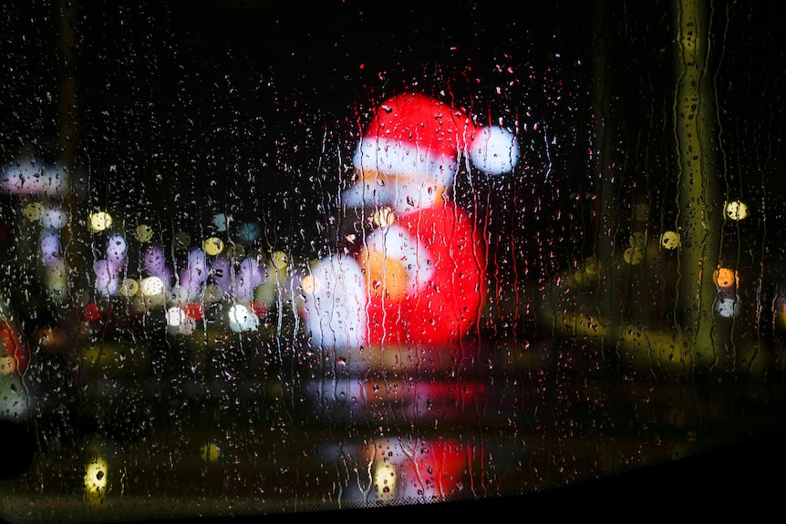 a large santa claus figure can be seen in Naples through rain drops on a car window