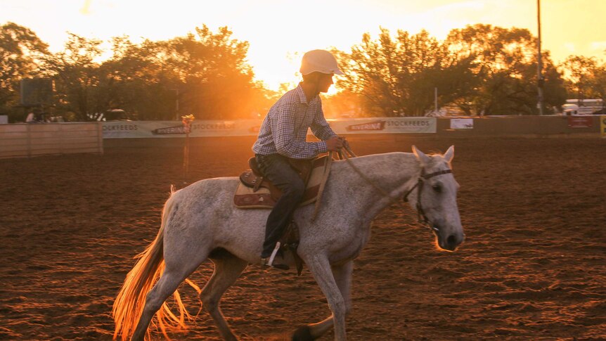 A campdrafter on horseback moves in front of an orange sky at the national titles.