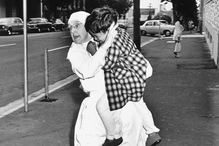 A nun rushes down the street carrying a child.