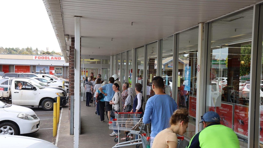 20 people line up outside a supermarket.