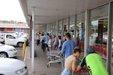 20 people line up outside a supermarket.