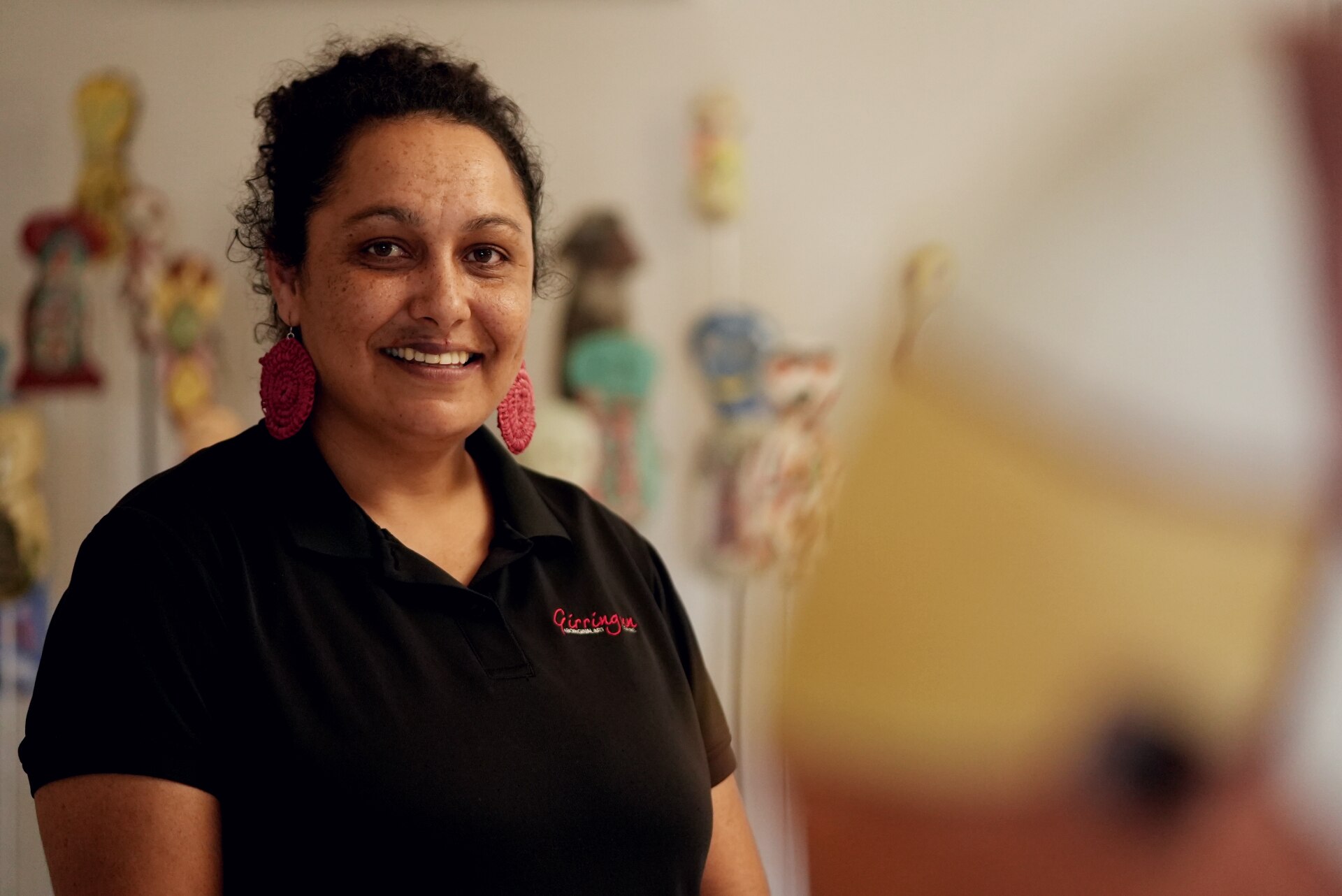 A smiling woman standing in art gallery with ceramic figures behind her.
