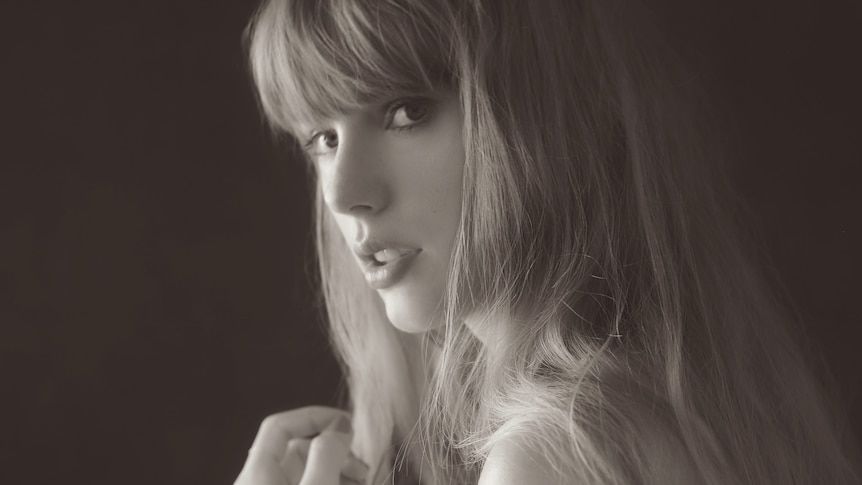 Taylor Swift in a black and white image, not smiling, looking over her shoulder, long blonde hair