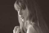 Taylor Swift in a black and white image, not smiling, looking over her shoulder, long blonde hair