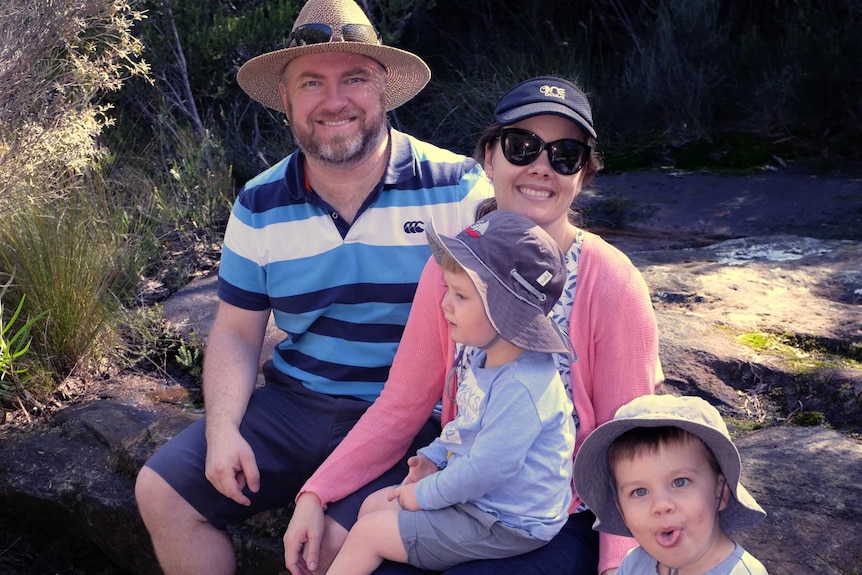 Alex and his wife sitting with their two sons on a bushwalk.