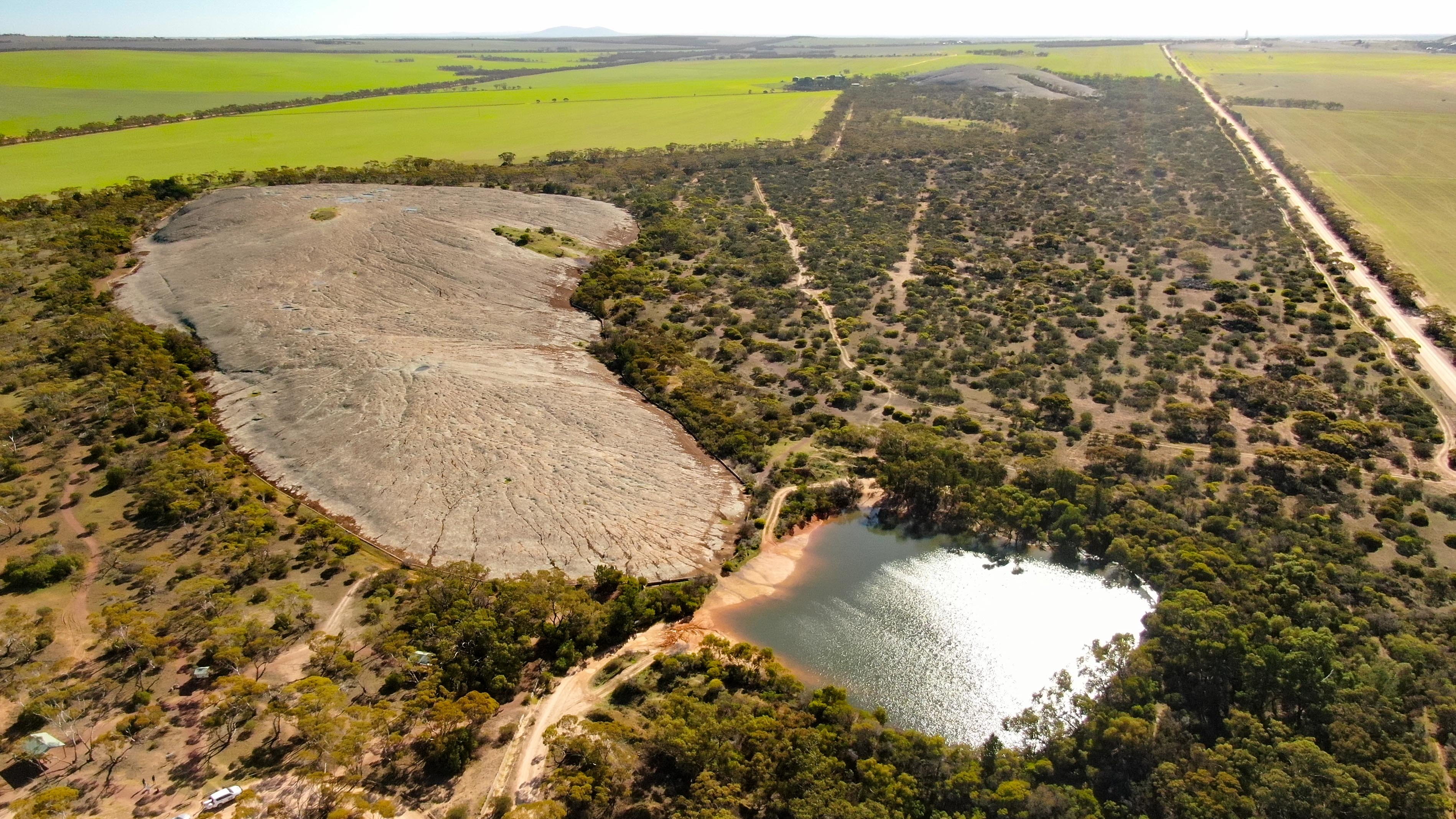 Huge rock dome rising from the flat landscape with a water reservoir at one end