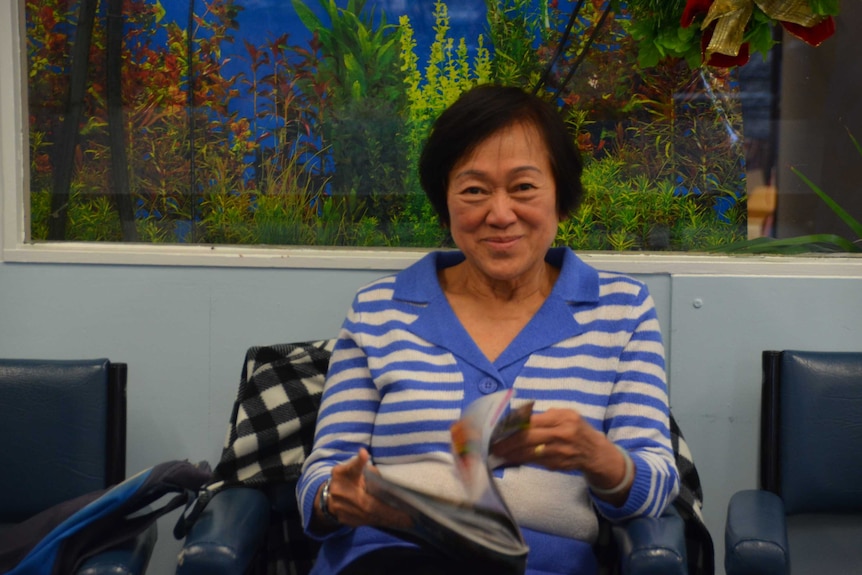 A woman sits with a news paper, a glass aquarium with plants behind her.