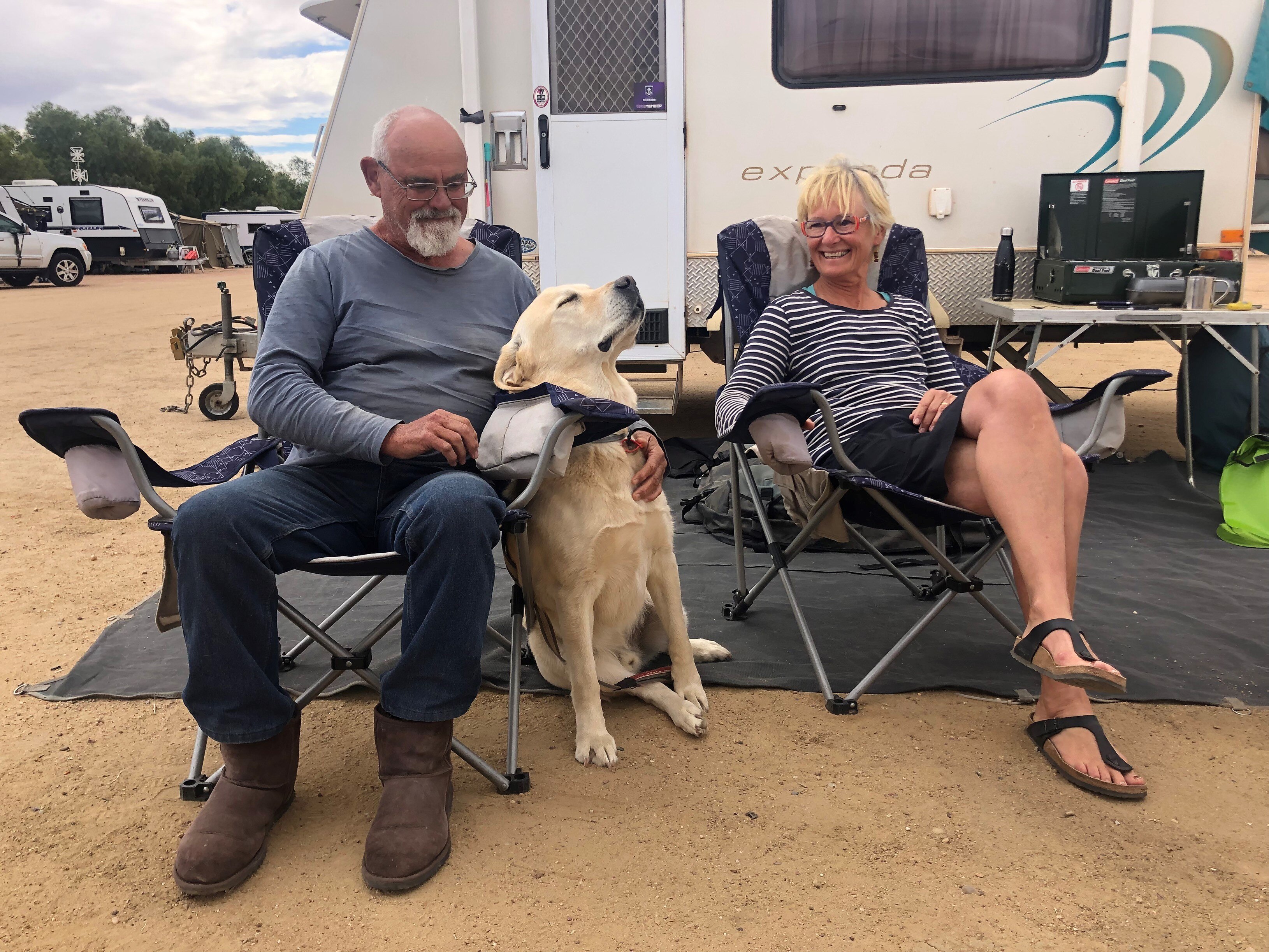 Couple sit in front of their caravan giving their labrador lots of love.