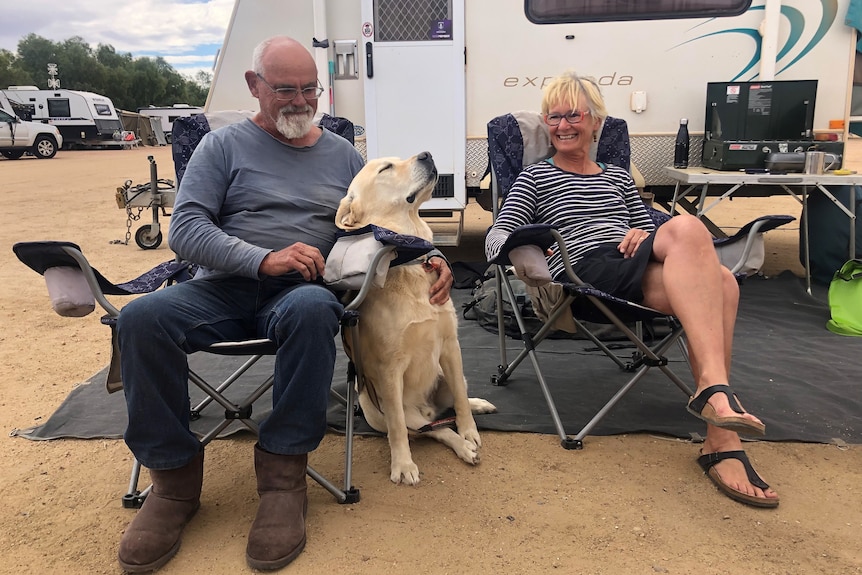 Couple sit in front of their caravan giving their labrador lots of love.