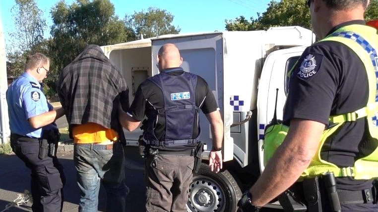 Police officers lead a handcuffed suspect into a waiting police vehicle.