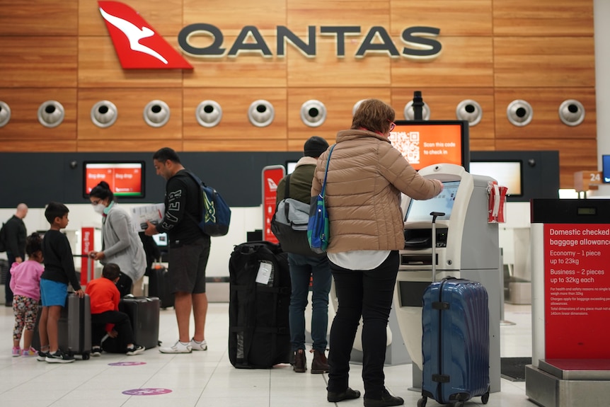 People with suitcases using computer terminals at an airport with a Qantas sign behind them