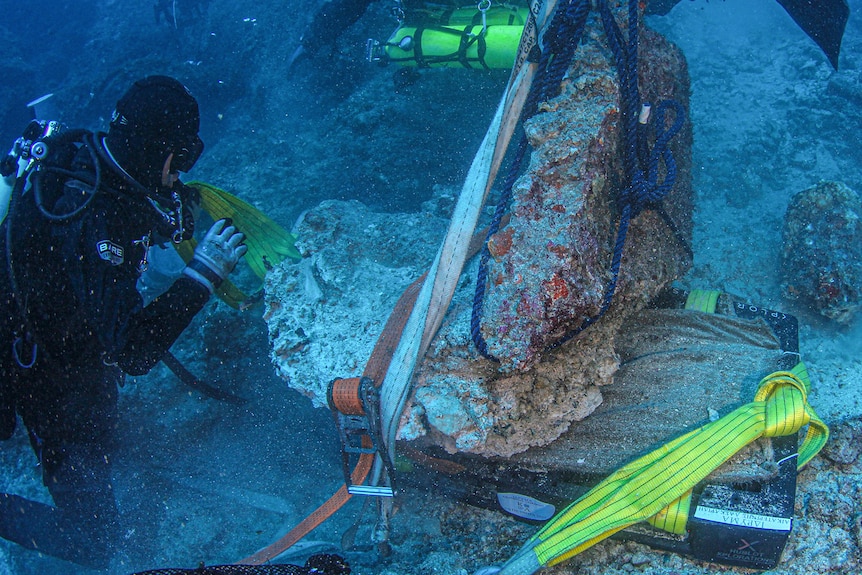 A diver wearing scuba gear examines a marble rock.