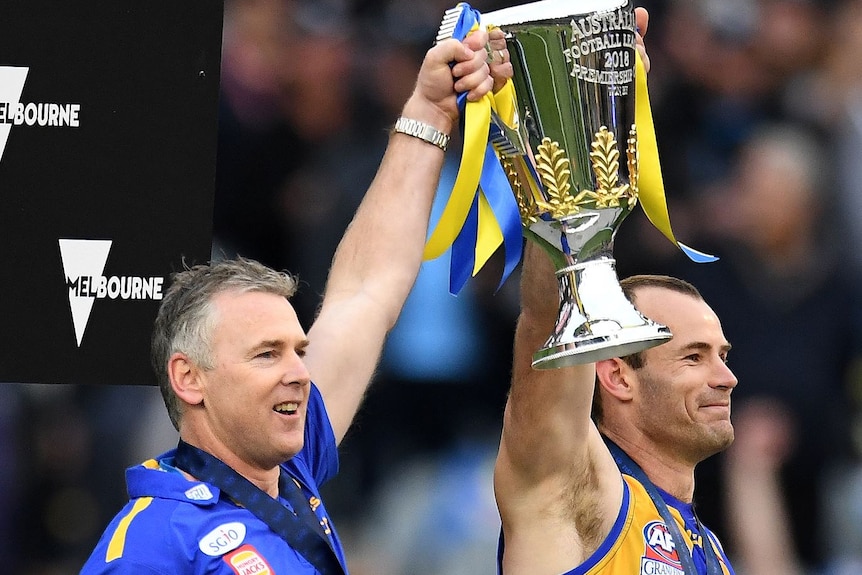Two men lift a large silver trophy over their heads. 