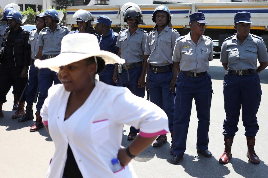 A woman in a white coat standing with her hands on her hips in a line of police officers