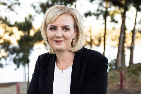 A woman with blonde hair smiles. She is wearing a black jacket and white shirt.