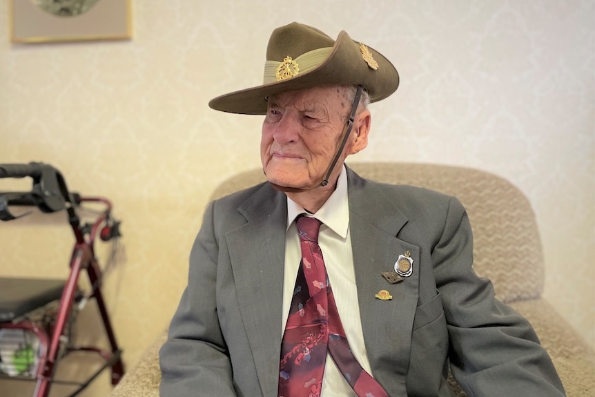 An elderly man sits with an army hat on