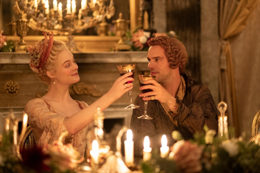 A film still of Elle Fanning and Nicholas Hoult wearing period costumes, and clinking goblets.