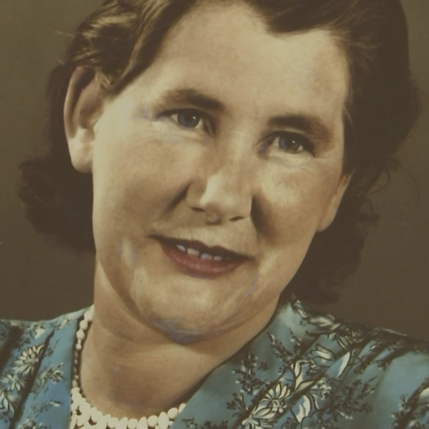 An old framed photograph of a middle-aged woman with brown hair, wearing a string of pearls. 