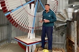A man stands in front of a red-and-white windmill he restored
