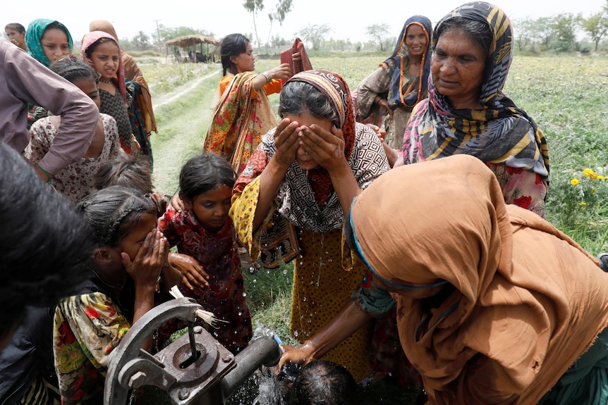 Women and children washing their face at a hand pump.