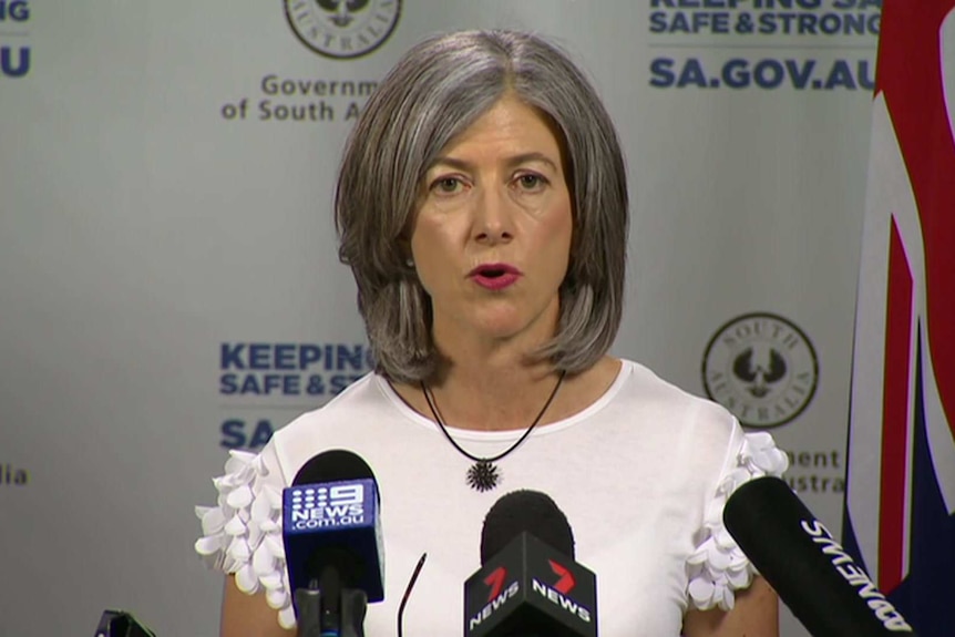 A woman with grey hair wearing a white top in front of an SA Government banner