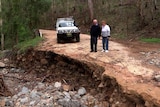 An elderly couple inspect damage to a dirt road which has left a large crater.