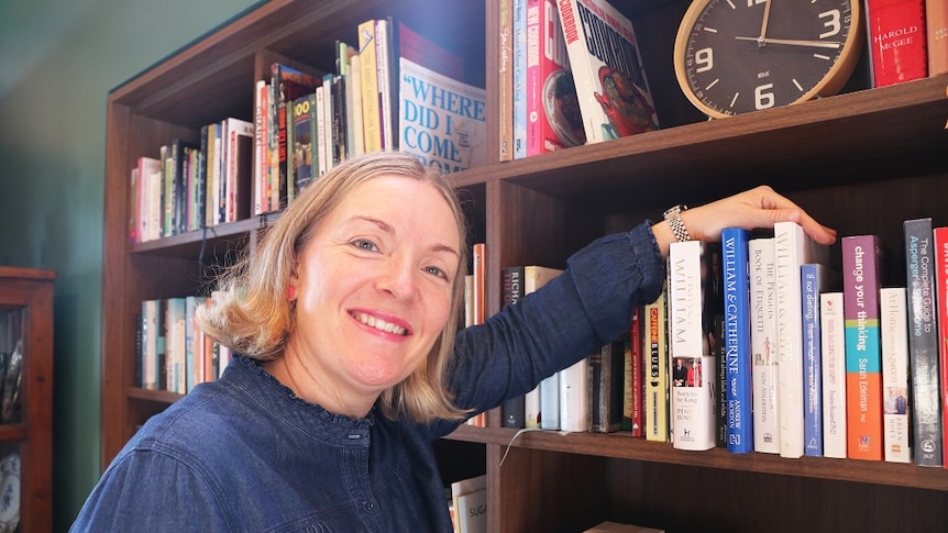 A woman smiling standing in front of a bookshelf