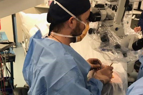 A man looks through microscopic equipment as he performs eye surgery on patient