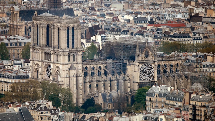 The Notre Dame Cathedral is seen from a distance, showing massive fire damage